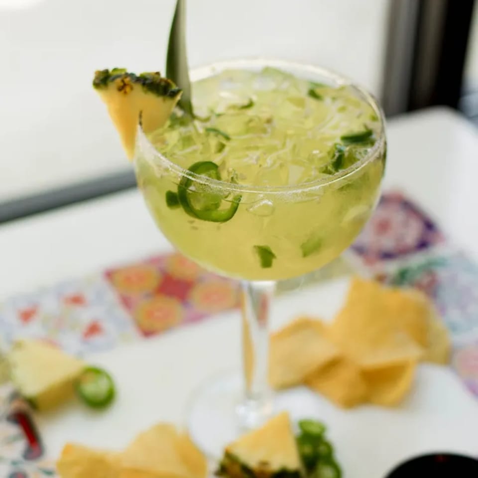 A Pedros Tacos & Tequila margarita with pineapple and jalapeño slices, surrounded by tortilla chips.